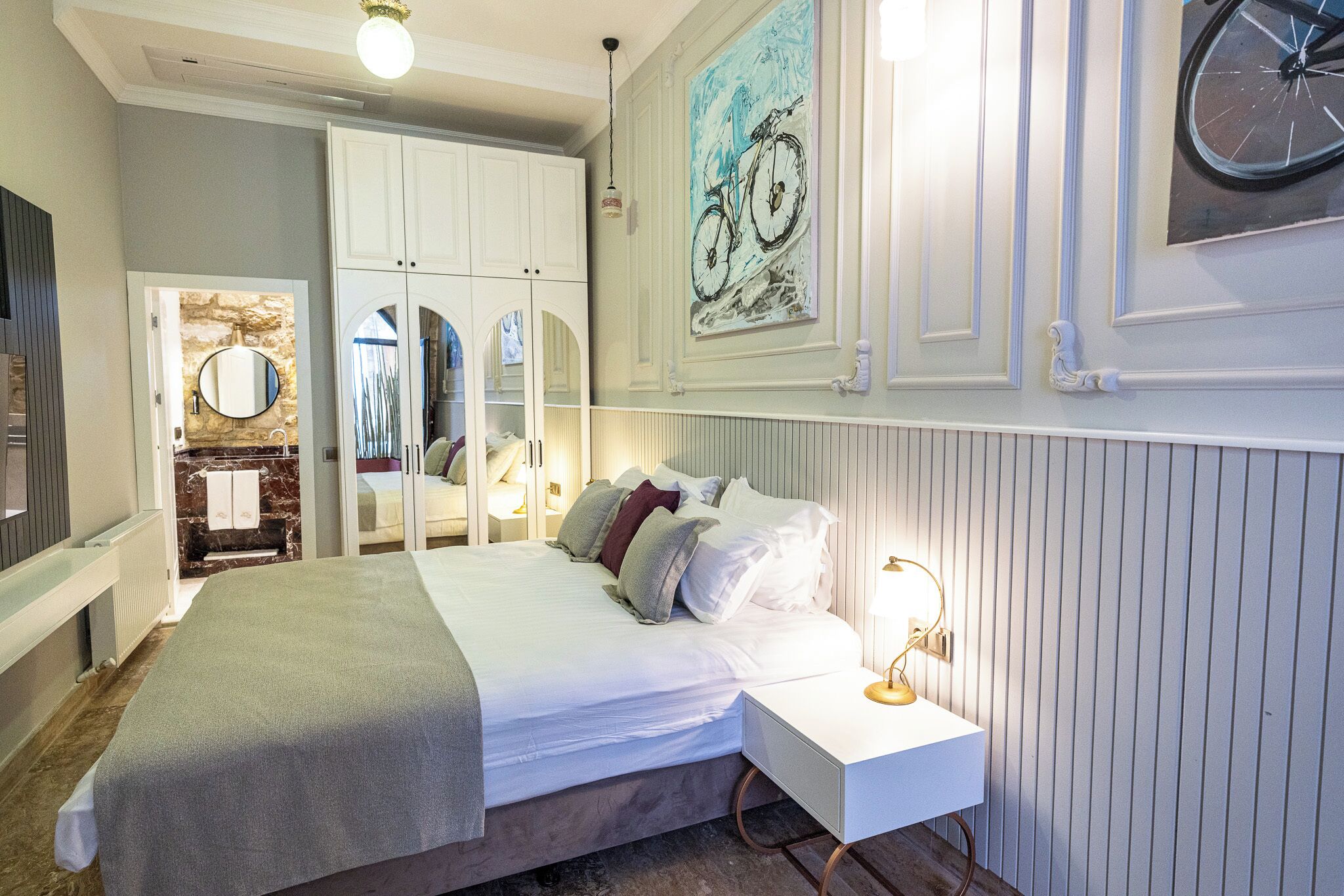 A bedroom with a bed, bedside table, and a mirror. There is a wardrobe with a mirror and a door.