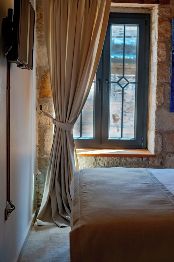 Un dormitorio con cama, ventana con cortinas, pared de piedra y televisor instalado en la pared.