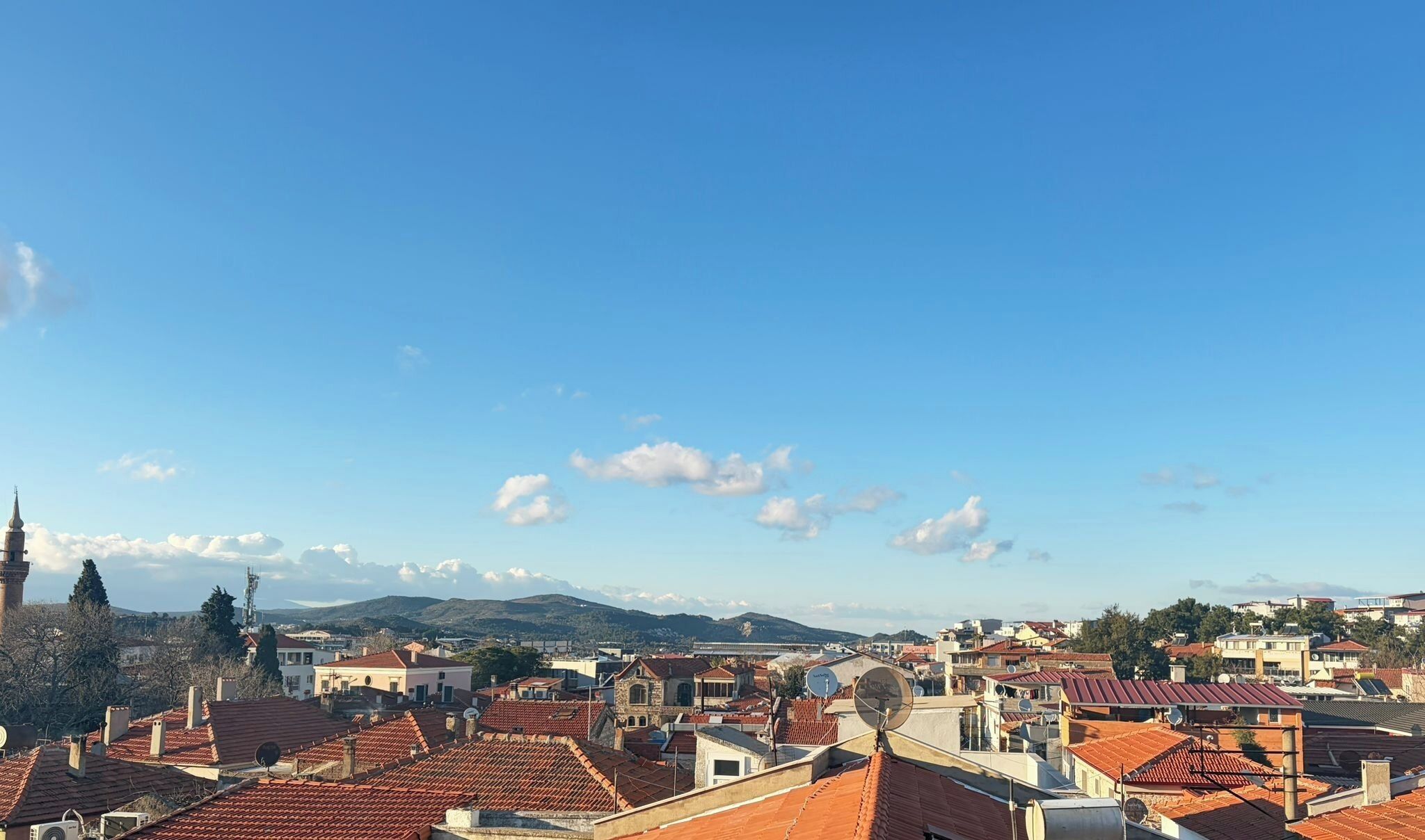 Uma cidade com telhados vermelhos, uma torre imponente e montanhas ao longe.