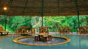 A circular pavilion with a thatched roof, surrounded by wooden tables and chairs, and a central water feature. - Penginapan Alam DGlorious CraterKamojang (Mekarwangi)