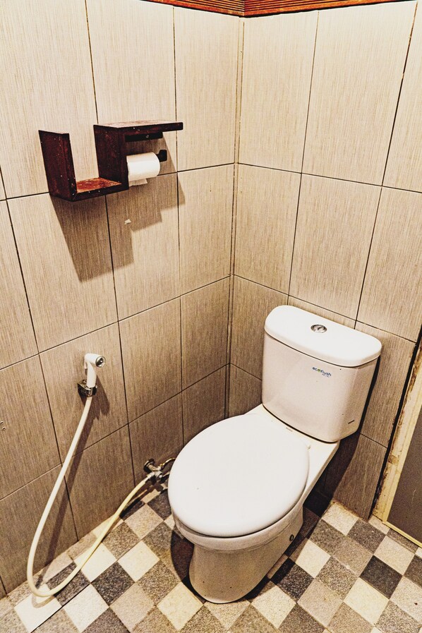 Une petite salle de bain avec des toilettes, une étagère avec un porte-rouleau de papier toilette et un carrelage à carreaux.