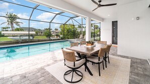 Un espacio moderno para comer al aire libre, con piscina, ventanas amplias y ventilador de techo.