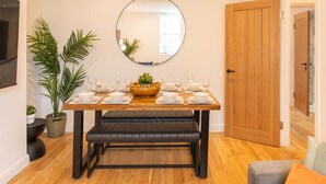 A dining area with a wooden table set for six, a round mirror above, and a bench in front. - Host Stay Princes Place Hideaway IV (Liverpool)