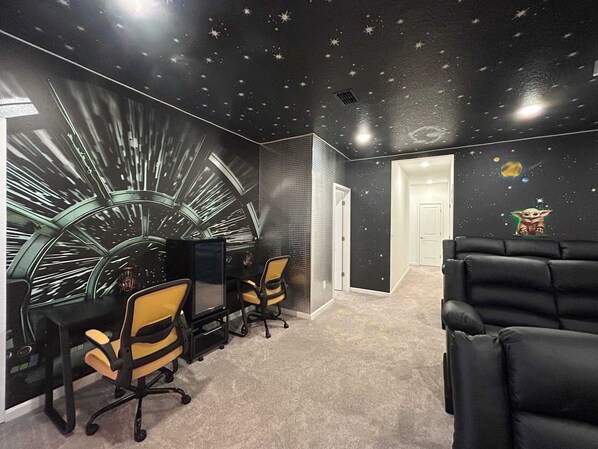 Une pièce avec un décor mural sur le thème de l’espace, un bureau avec deux chaises et un canapé en cuir noir.