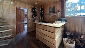 Interior de fusta amb una prestatgeria de vi, una barra amb diferents objectes i una finestra que mostra vistes d'arbres.