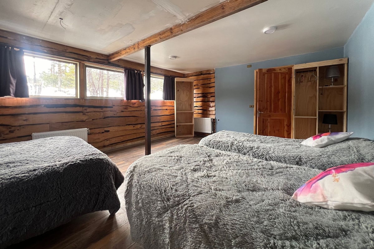 Een kamer met twee bedden, houten wanden, een groot raam en een kledingkast.