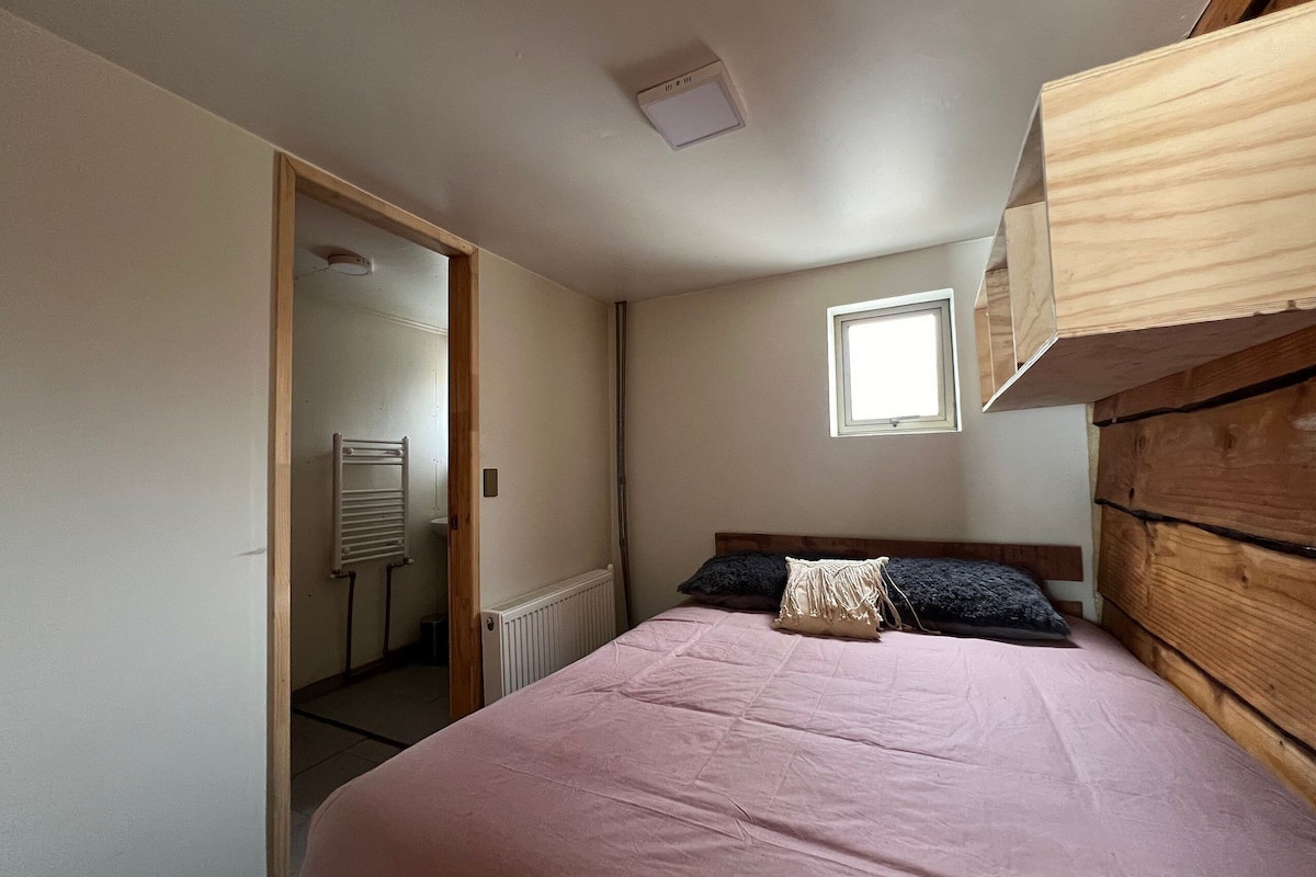 Een slaapkamer met een bed, een raam, een radiator en een houten hoofdeinde.