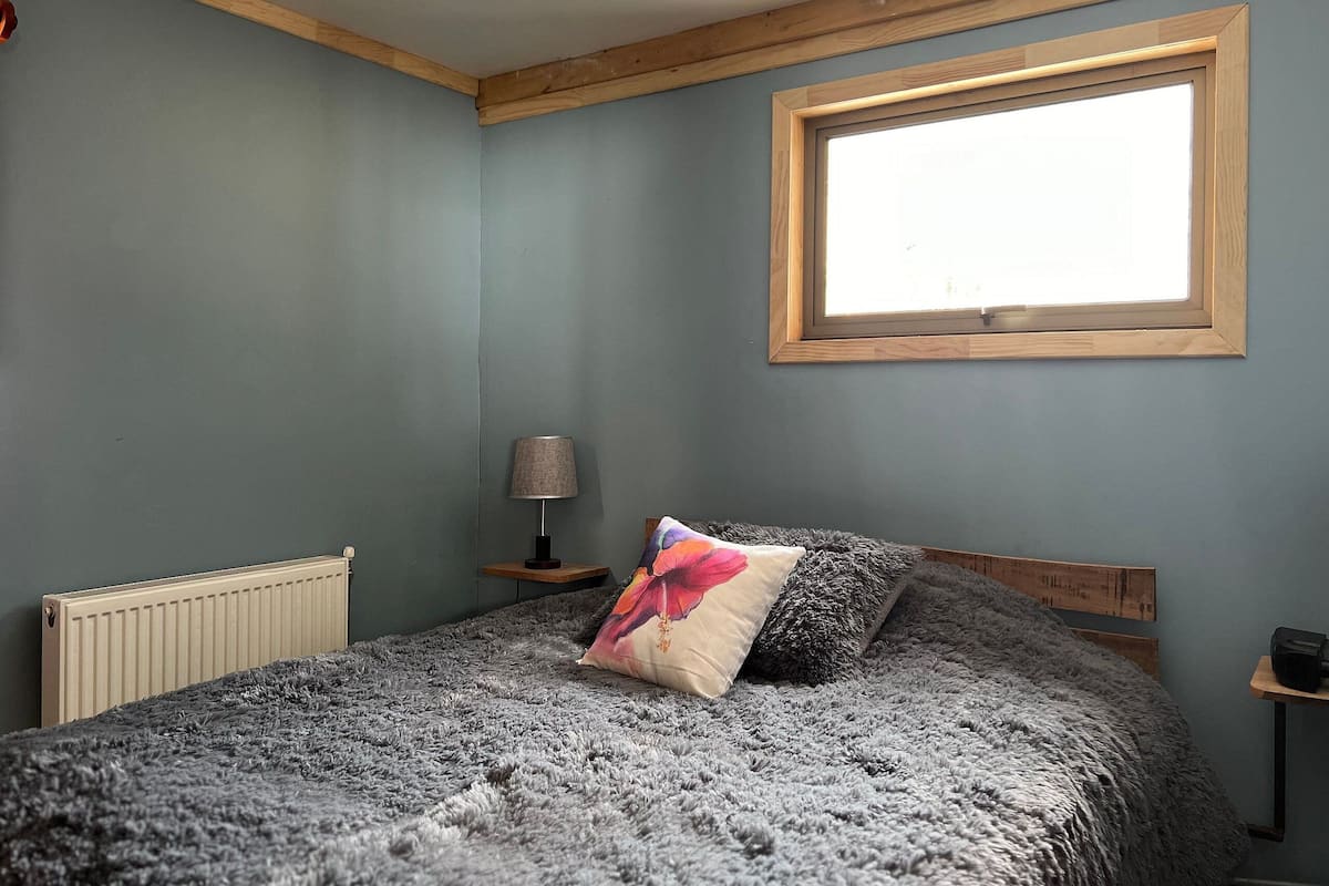 Een slaapkamer met een bed, een raam, een radiator en een lamp.