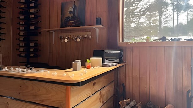 Interior d'una cabana de fusta amb una cuina, ampolles de vi, un microones i vistes a arbres per una finestra.