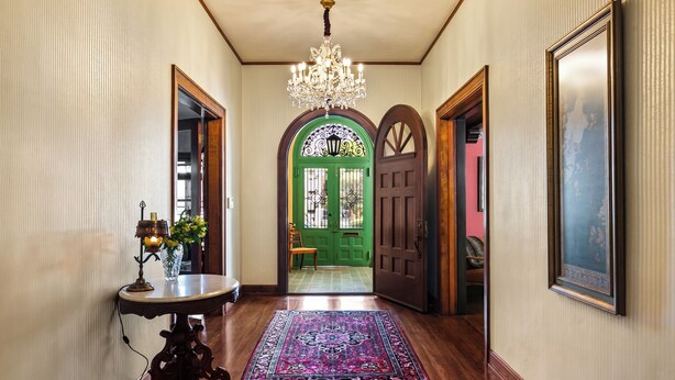 A hallway with a chandelier, a green door, and a patterned rug.