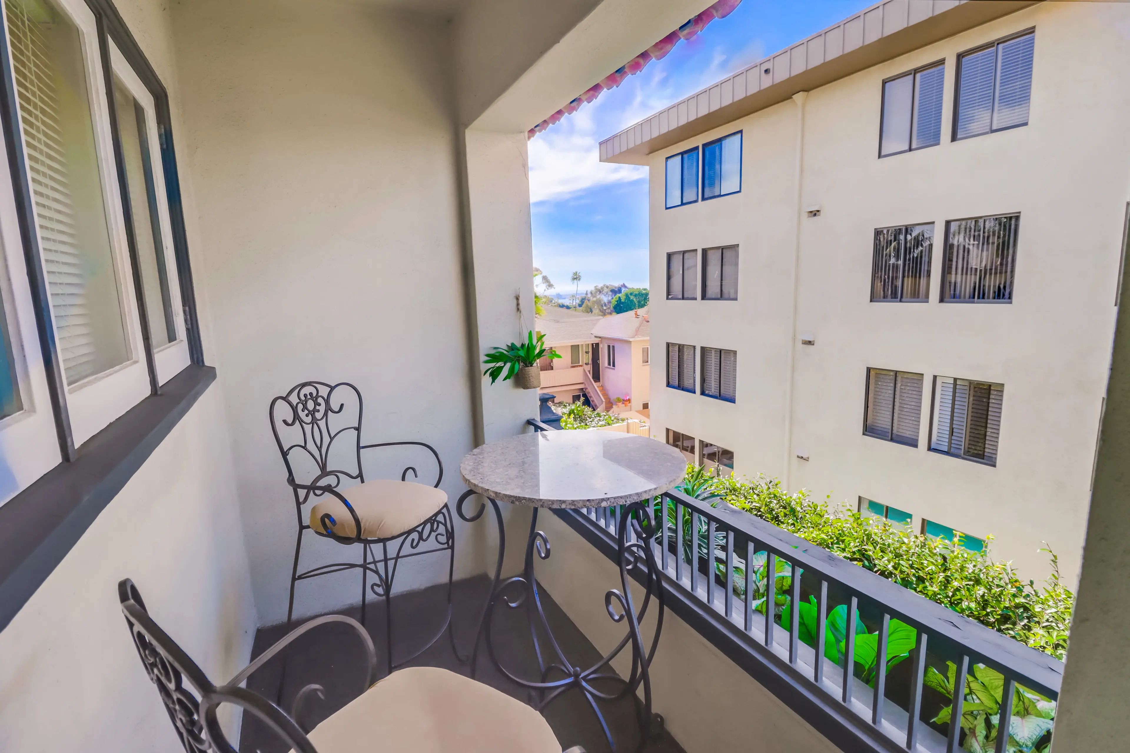 A balcony with a round table and two chairs, overlooking a residential area with multiple buildings.