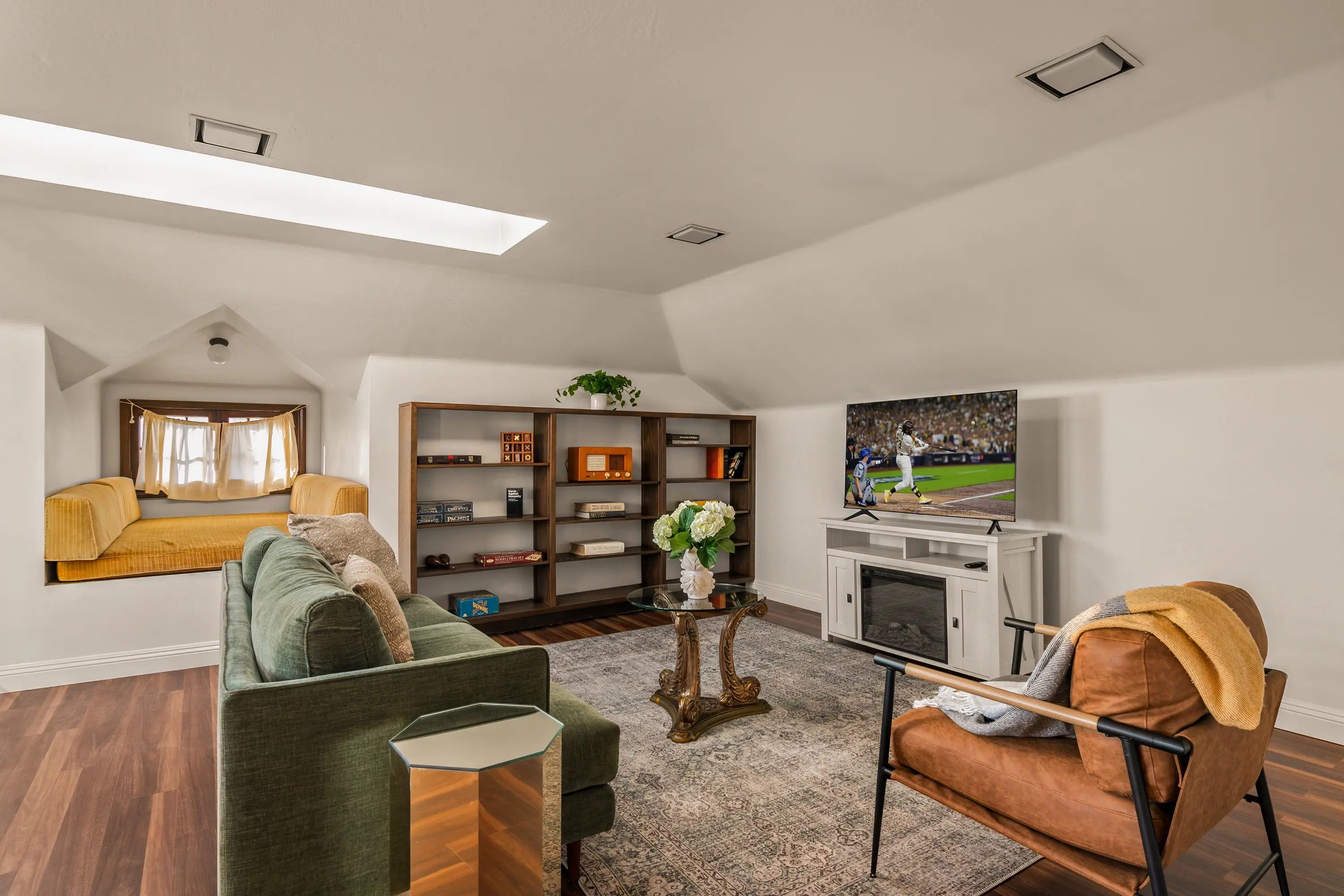 A modern living room with a high ceiling, a built-in bookshelf, a television, and a seating area with a sofa and armchairs.