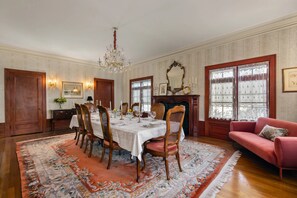 Une salle à manger avec une grande table dressée pour six personnes, entourée de chaises, d’un lustre et d’une cheminée.