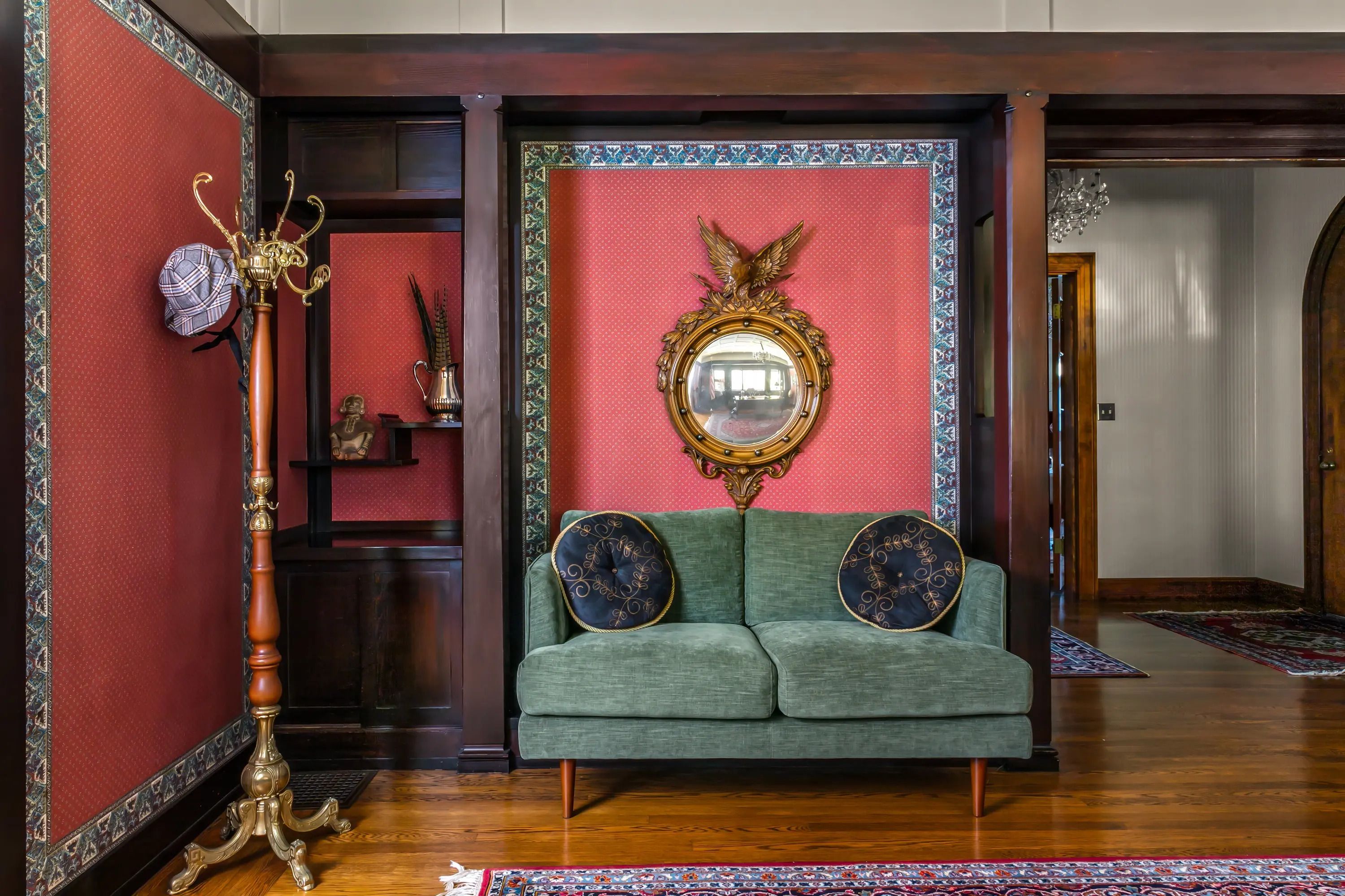 A room with a green sofa, a decorative mirror, and a patterned rug.