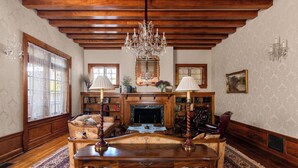 A traditional living room with a wooden ceiling, a chandelier, a fireplace, and a large rug.