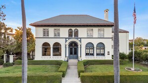 A two-story building with a symmetrical facade, a central entrance with a double door, and a small balcony above the entrance.