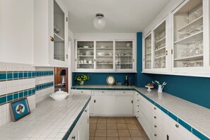 A kitchen with white cabinets, a blue accent wall, and a tiled backsplash. - The Coulter House by Gather: Historic San Diego Estate w/ Ocean Views (San Diego)