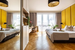 A hotel room with two beds, a desk, a chair, and a large window with curtains.