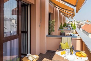 Un balcón con mesa dispuesta para el desayuno, una ventana con cortinas y vistas a la ciudad.