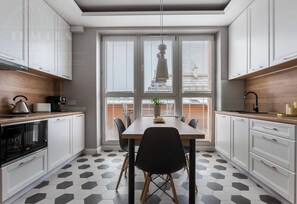 Una cocina moderna con armarios blancos, un comedor con mesa negra y un piso de baldosas hexagonales.
