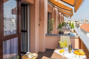 A balcony with a table set for breakfast, a window with curtains, and a view of the cityscape.