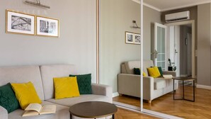 Een moderne woonkamer met een bank, een ronde salontafel en een grote spiegel die de kamer weerspiegelt.