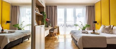 Habitación de hotel con dos camas, un escritorio, una silla y un ventanal con cortinas.