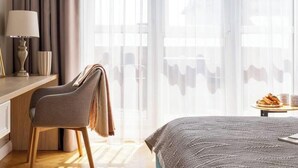A hotel room with a bed, a desk, a chair, a small table with a plate of food, and a window with curtains. - Feniks Stunning 2-bed apartment with 3 terraces (Kraków - Feniks)