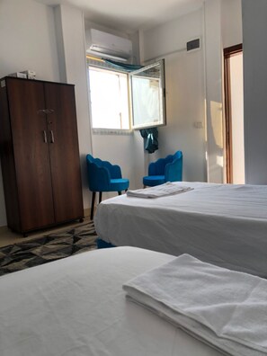 Una habitación de hotel con dos camas, un armario, una ventana con cortinas y una mesita.