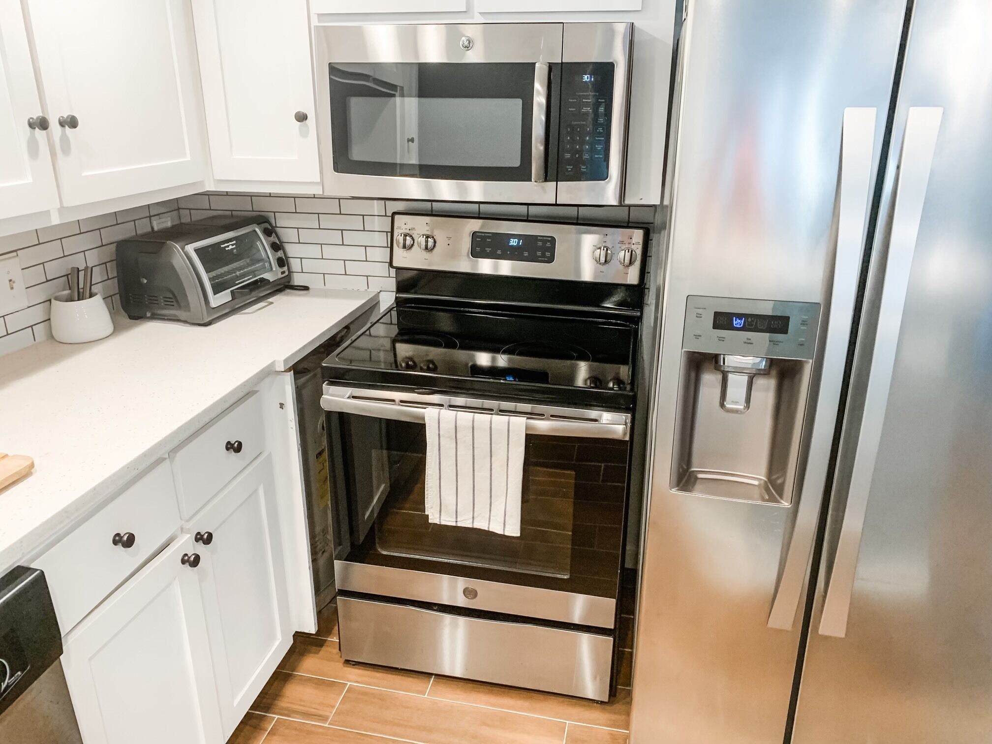 A compact kitchen with a built-in microwave, a toaster, a stainless steel oven, and a refrigerator.