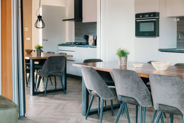 A modern kitchen with a wooden dining table, grey upholstered chairs, and a built-in oven.