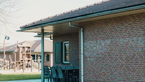 Un bâtiment en briques doté d’un patio couvert, d’un espace extérieur aménagé pour s’asseoir et d’une aire de jeux en arrière-plan.