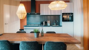 A modern kitchen with a wooden dining table, grey chairs, a built-in oven, and pendant lighting.