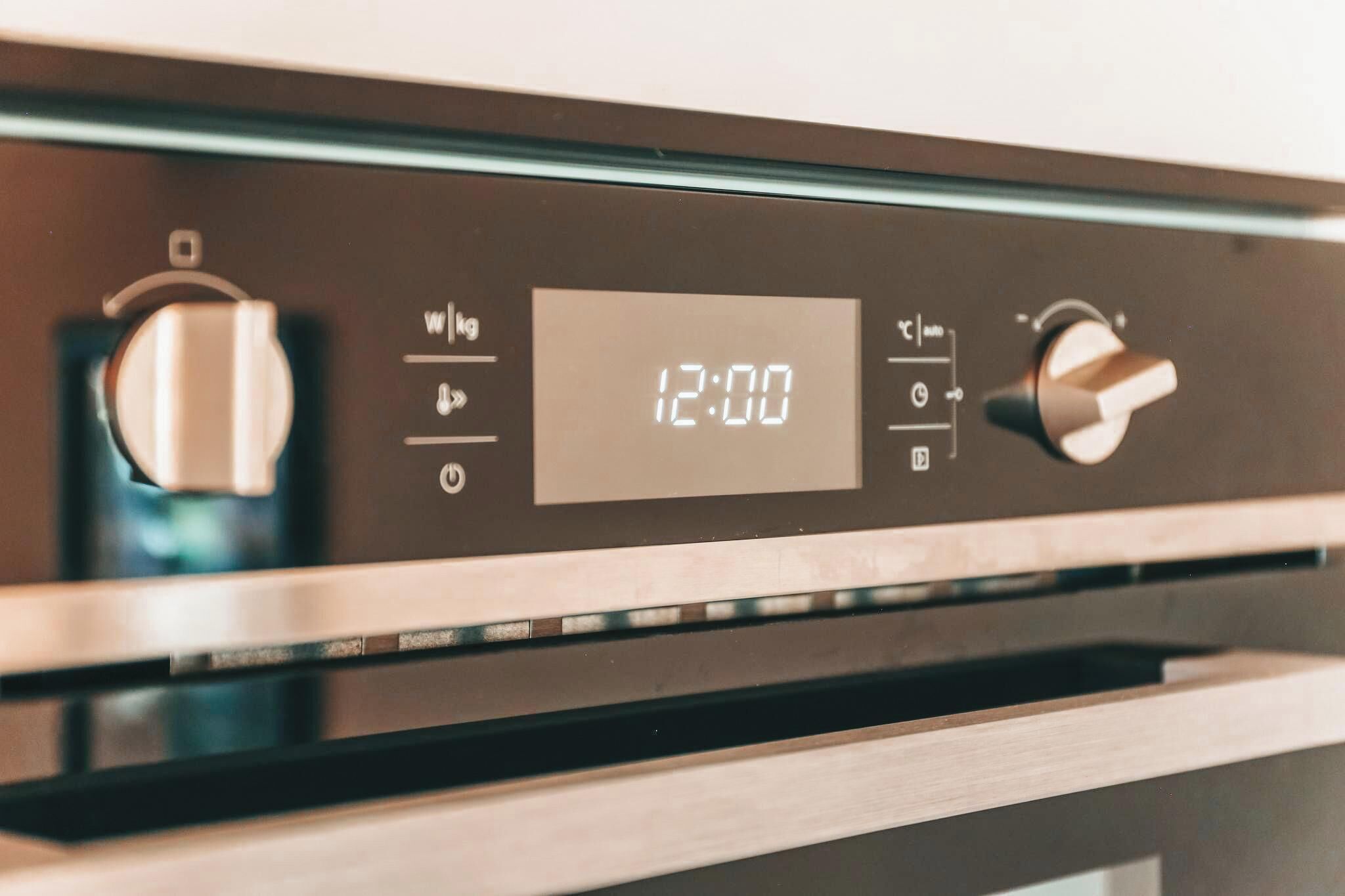 Een digitale klok op een keukenapparaat, waarop 12:00 uur staat.