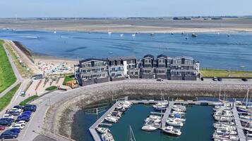 Een jachthaven met afgemeerde boten, een gebouw met meerdere balkons en een zandstrand met parasols.