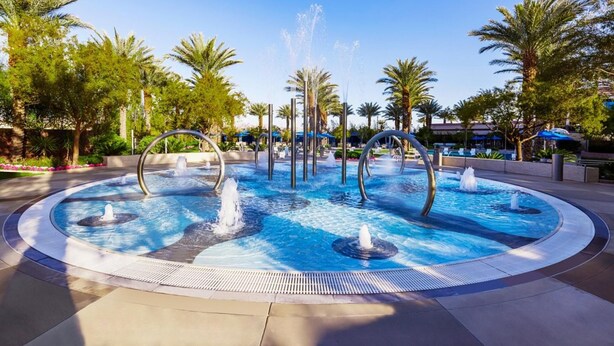 Una piscina circular con múltiples fuentes y palmeras alrededor.