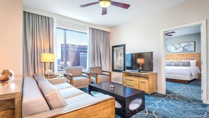Habitación de hotel con sofá, sillas, televisión, escritorio, cama y vistas a la ciudad.