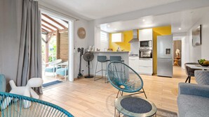 A modern living room with a sofa, a chair, and a dining area with a table and chairs. - Golden Oasis - One Bedroom Apartment, Sleeps 2 (Le Marin)