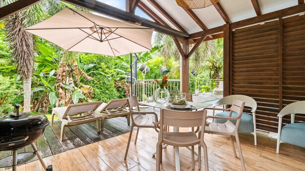 An outdoor patio with wooden flooring, a grill, and a table set for dining. - Golden Oasis - One Bedroom Apartment, Sleeps 2 (Le Marin)