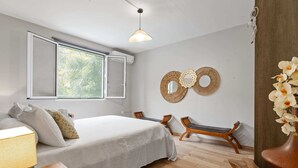 A bedroom with a bed, a window, a wall-mounted mirror, a wooden bench, and a decorative wall piece. - Golden Oasis - One Bedroom Apartment, Sleeps 2 (Le Marin)