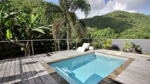 A wooden deck with a rectangular pool, surrounded by lush greenery and a mountainous backdrop. - Golden Oasis - One Bedroom Apartment, Sleeps 2 (Le Marin)