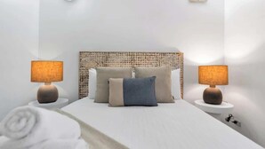 A neatly made bed with a headboard, two bedside lamps, and a rolled towel on the floor. - Leafy Solace—A Contemporary Cairns City Hideaway (Cairns)