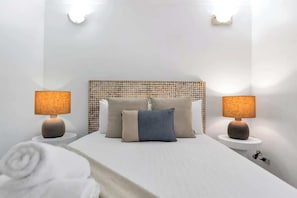 Un letto rifatto con un poggiatesta, due lampade sui comodini e un asciugamano arrotolato sul pavimento.
