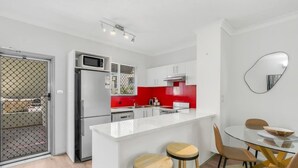 A modern kitchen with a white island, red backsplash, and stainless steel appliances. - Leafy Solace—A Contemporary Cairns City Hideaway (Cairns)