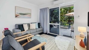 A modern living room with a grey sofa, a wooden bench, and a large window with curtains. - Leafy Solace—A Contemporary Cairns City Hideaway (Cairns)
