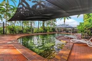 Una piscina con ombrellone, lettini e vegetazione tropicale.