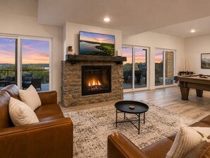 Een woonkamer met een stenen open haard, een pooltafel en een groot raam met uitzicht op een prachtig landschap.
