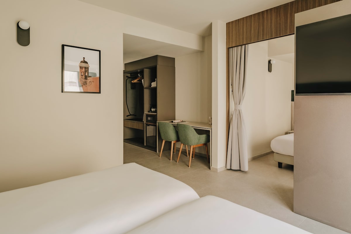 Una camera d'albergo con un letto, una scrivania con due sedie, un armadio e un bagno.
