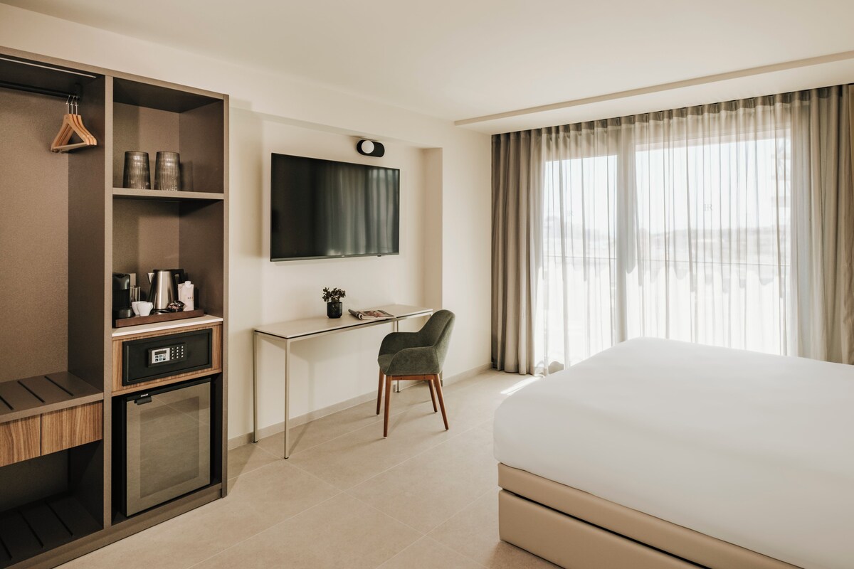 Une chambre d’hôtel comprenant un lit, un bureau avec une chaise, une télévision, un minibar et une armoire.