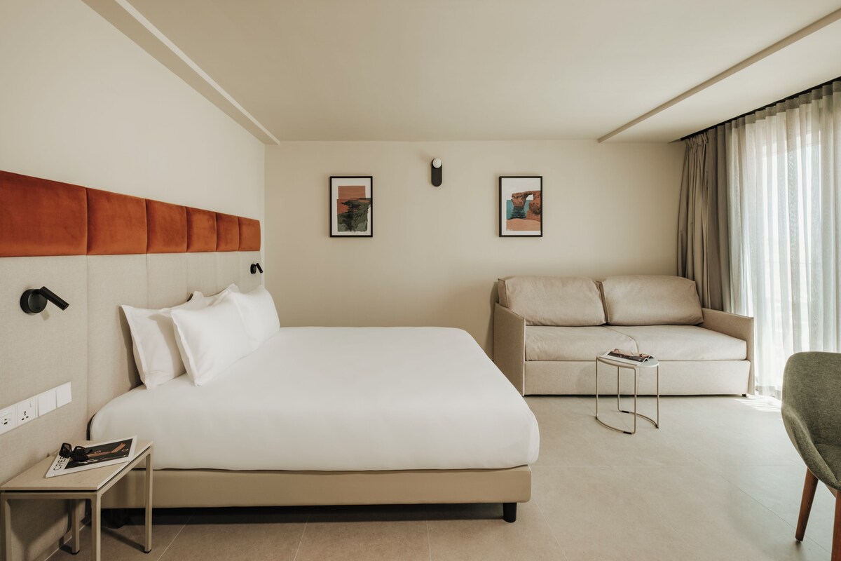 Une chambre d’hôtel moderne, dotée d’un grand lit, d’un canapé, d’une petite table d’appoint et de deux tableaux encadrés accrochés au mur.